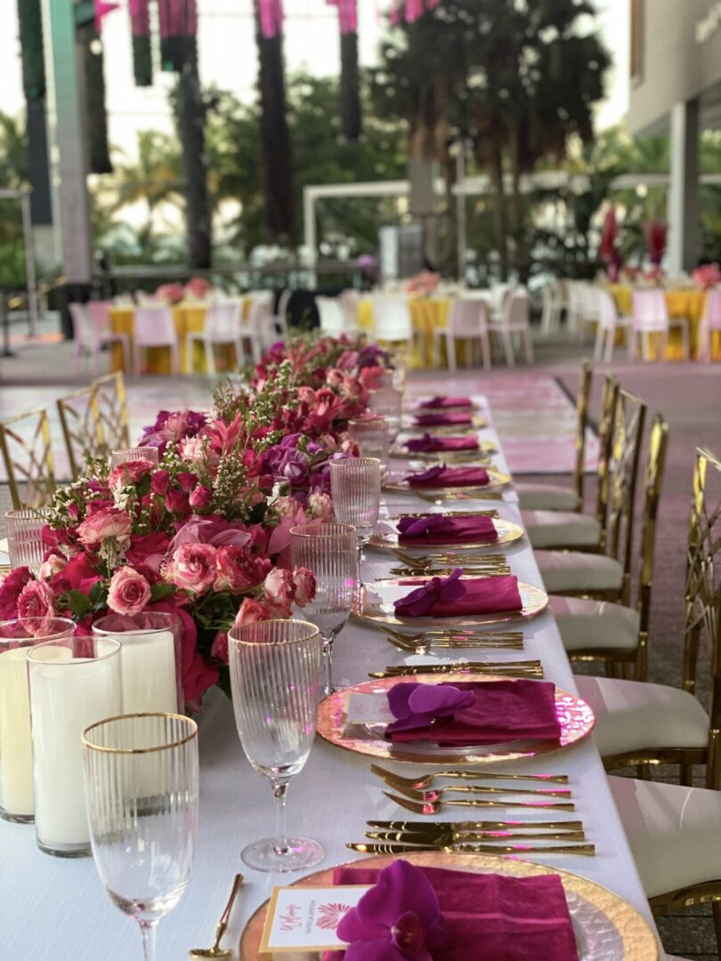 A long table with pink flowers and gold chairs.